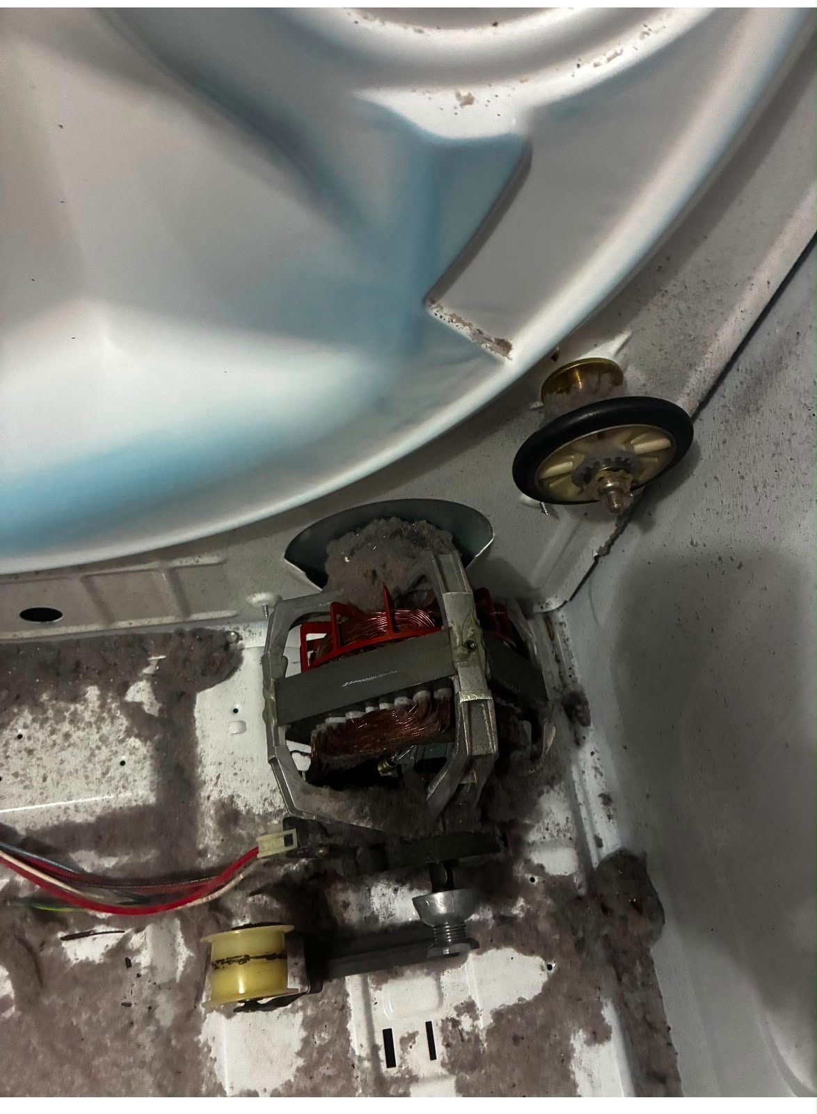 A dryer motor and idler pulley packed with lint before cleaning